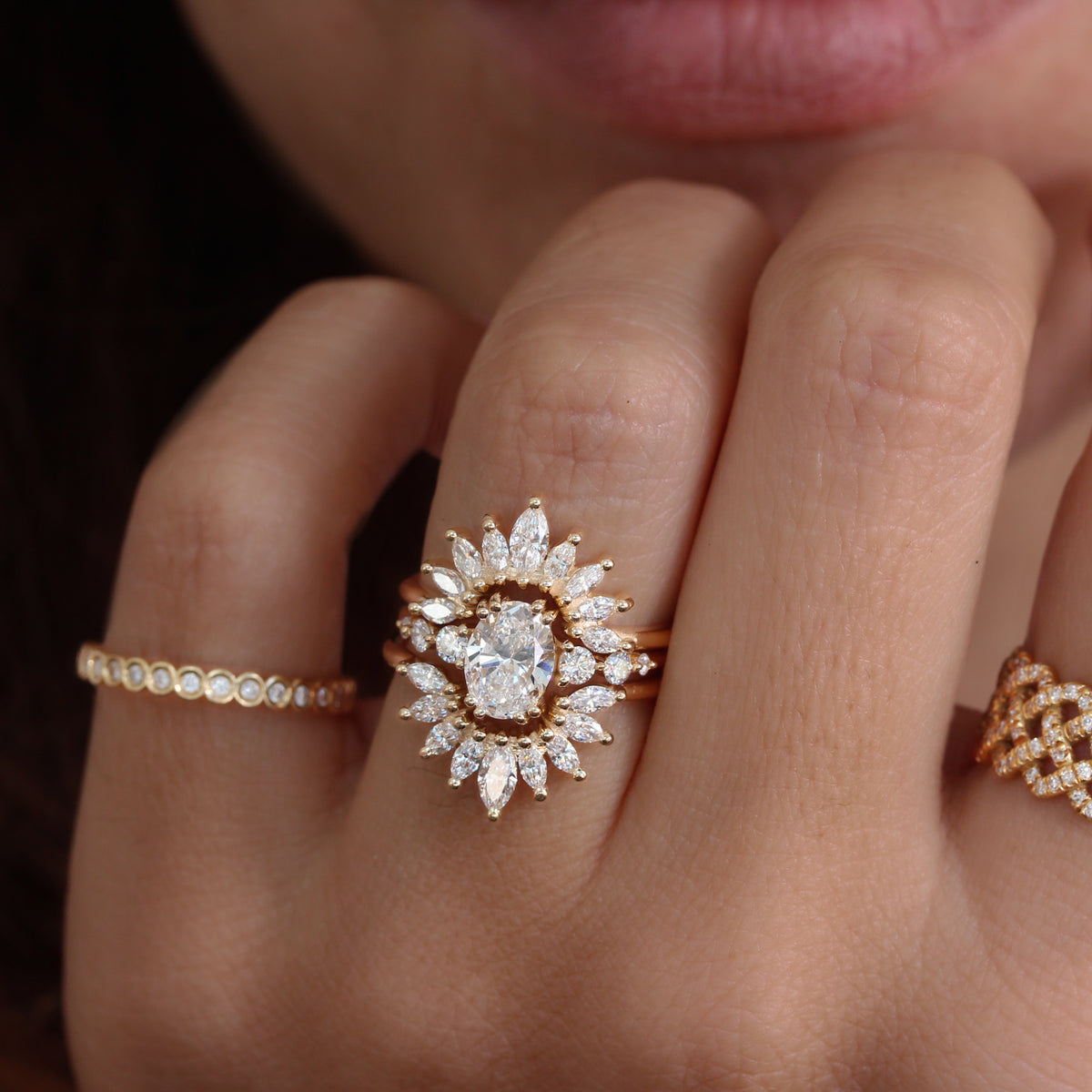 An oval diamond engagement ring with two marquise diamonds on a gold band, designed in a sunburst pattern.