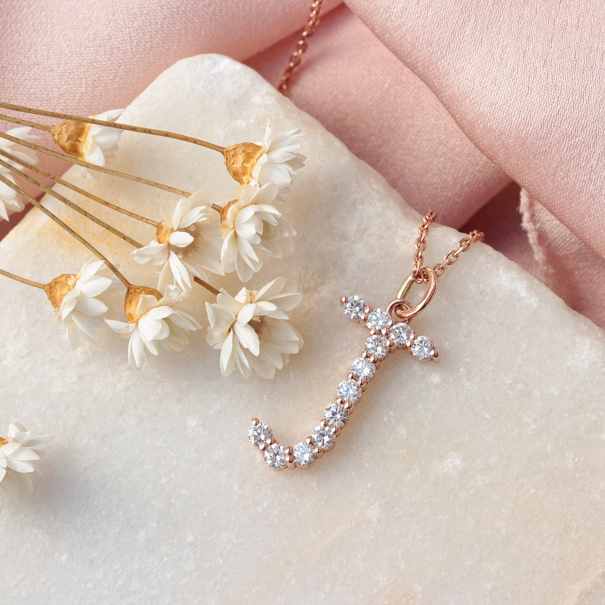 Jumbo Diamond Initial Charm 17mm Tall Rose gold necklace with diamond pendant on a marble surface with dried flowers.