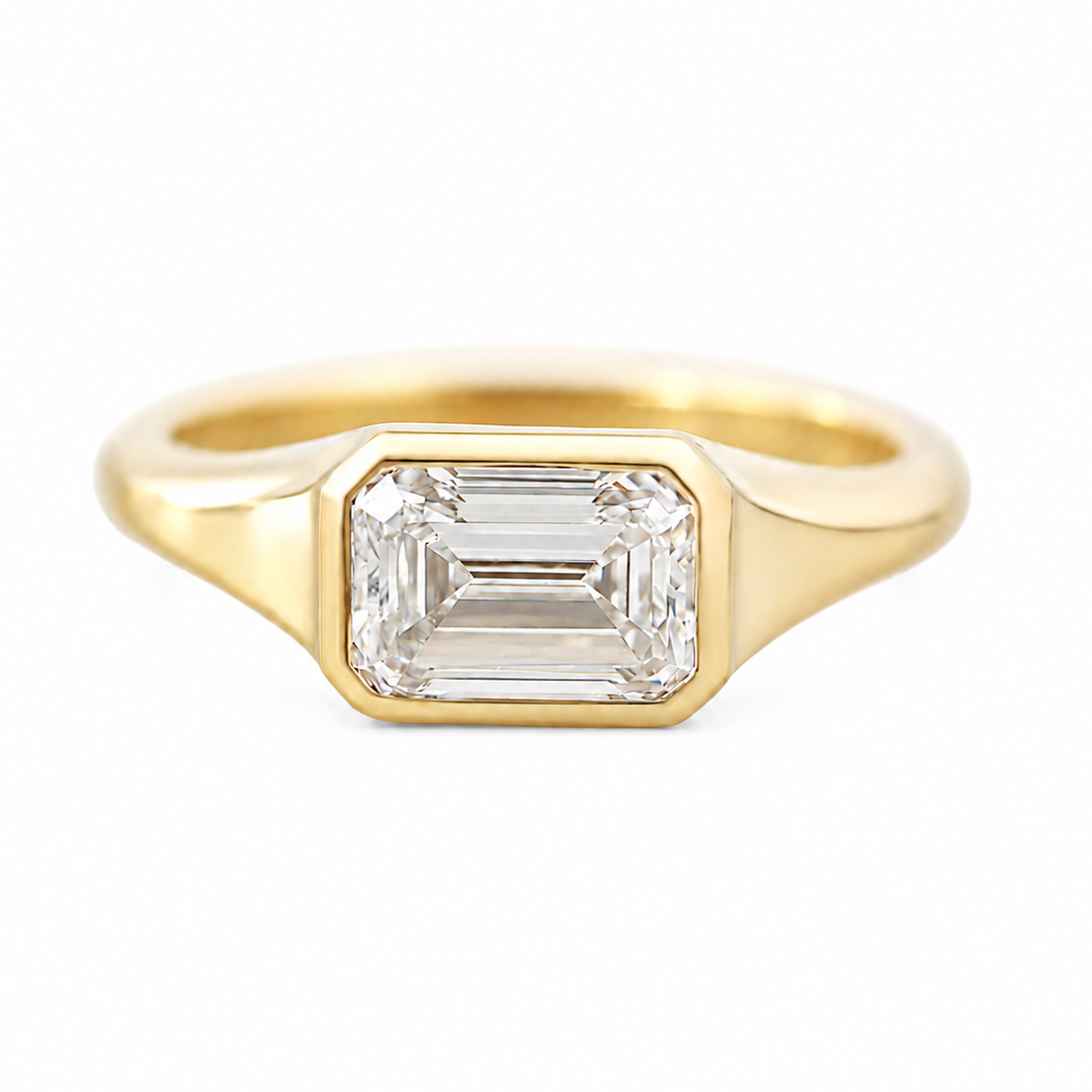 1.5CT EAST WEST solitaire engement ring, A yellow gold ring featuring a rectangular baguette-cut clear gemstone, set in a polished gold band against a plain white background.