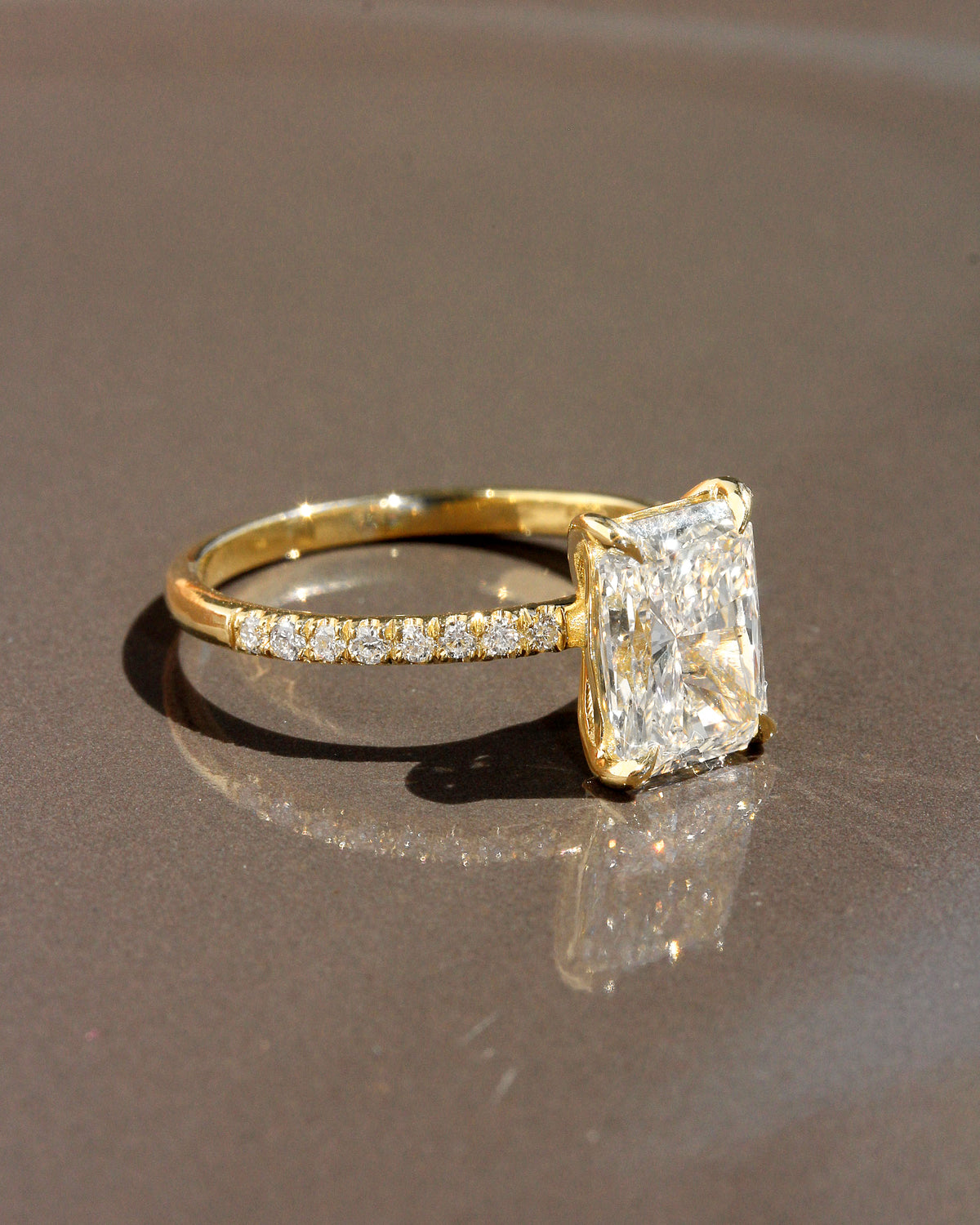 2 ct radiant-cut diamond engagement ring. A yellow gold engagement ring featuring a large rectangular radiant-cut diamond center stone, with a pavé-set diamond band, shown on a clean white background.