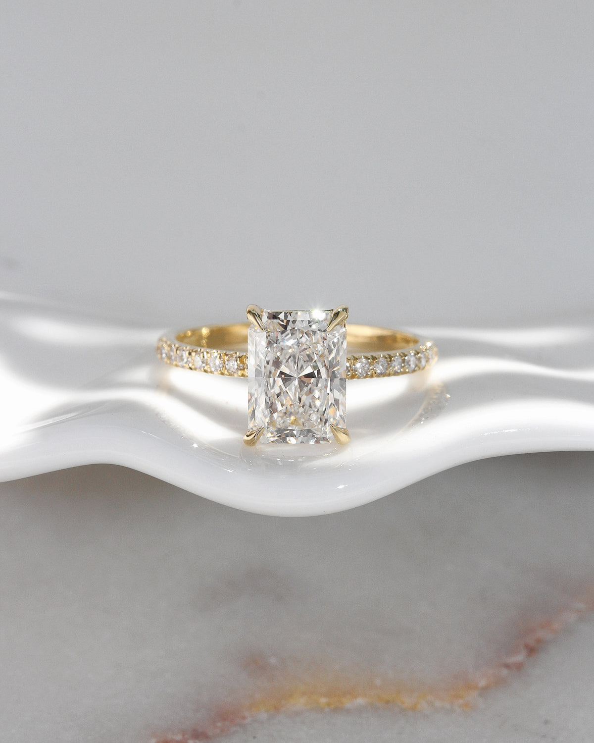 2 ct radiant-cut diamond engagement ring. A yellow gold engagement ring featuring a large rectangular radiant-cut diamond center stone, with a pavé-set diamond band, shown on a clean white background.