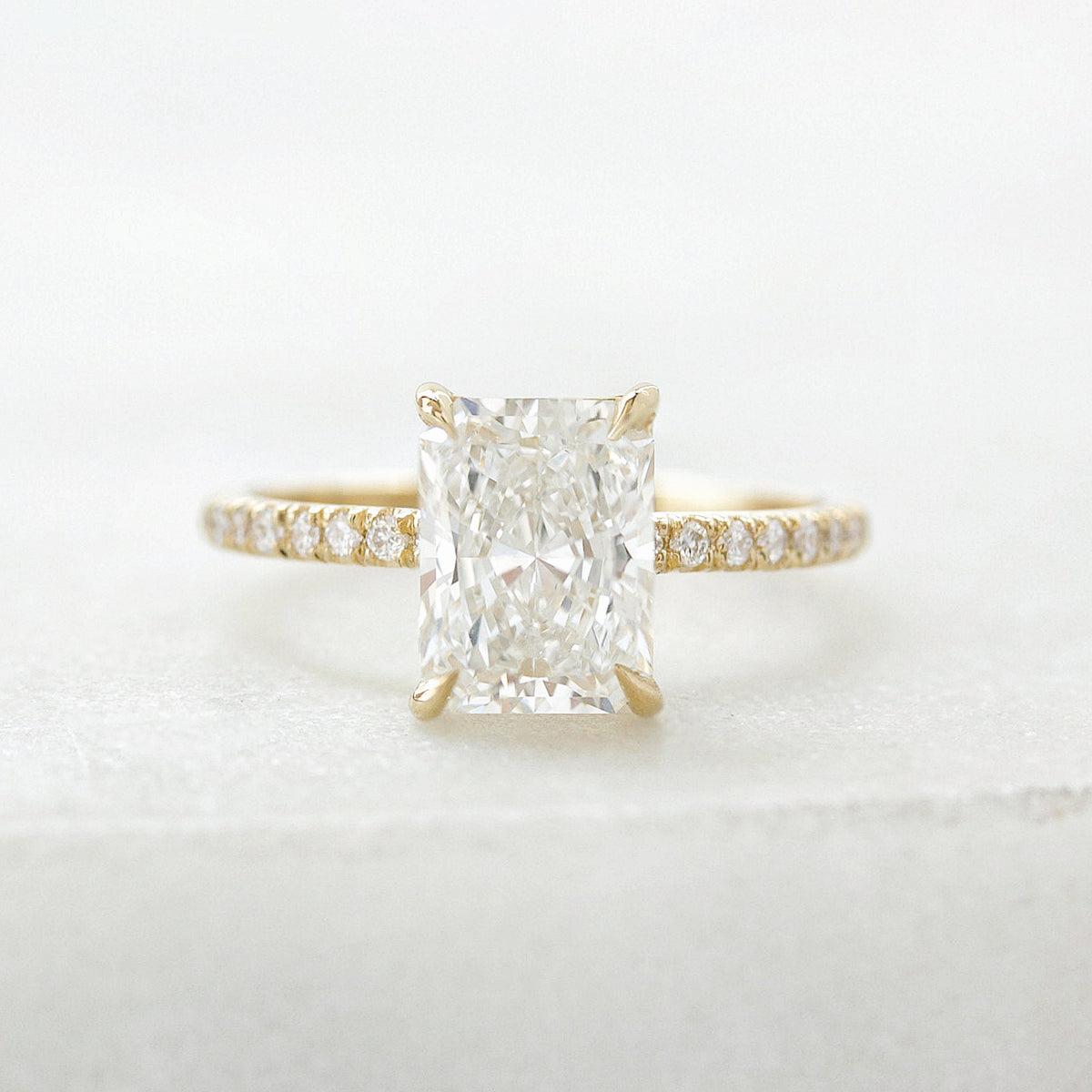 2 ct radiant-cut diamond engagement ring. A yellow gold engagement ring featuring a large rectangular radiant-cut diamond center stone, with a pavé-set diamond band, shown on a clean white background.