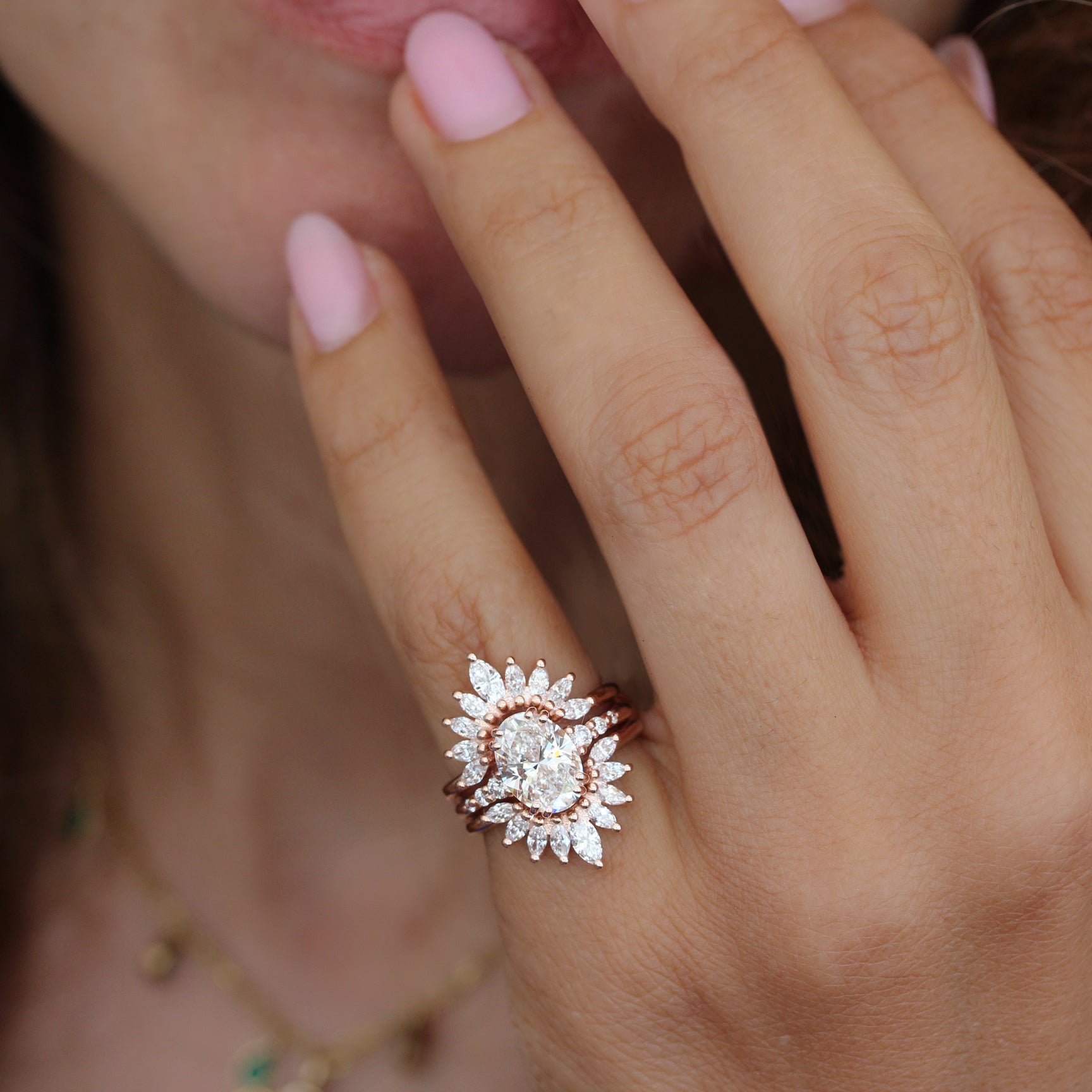2ct oval diamond engagement ring. A close-up lifestyle shot of a woman's hand wearing a rose gold ring with a diamond sunburst design, featuring a central round diamond surrounded by smaller diamond petals.