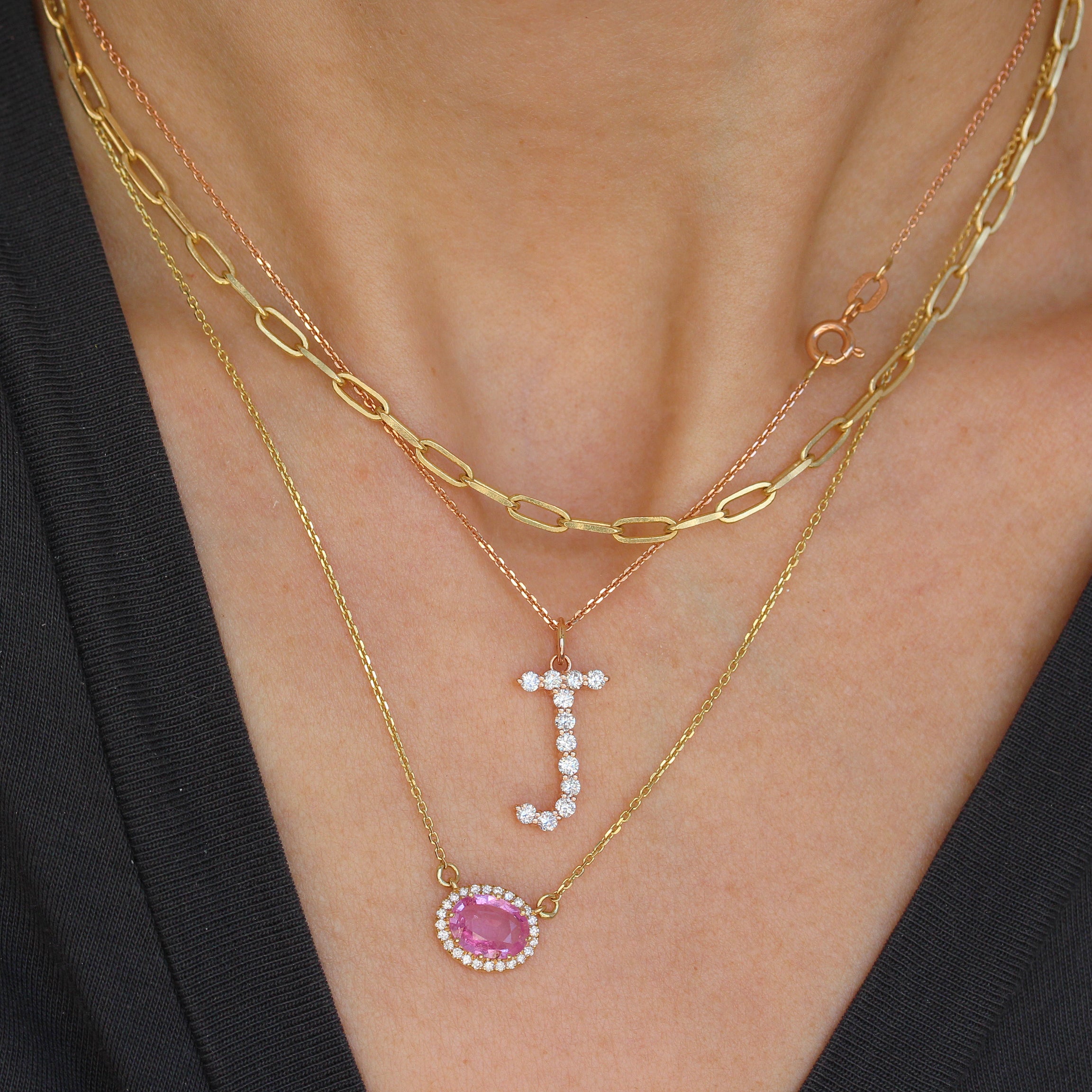 Jumbo Diamond Initial Charm 17mm Tall Gold necklaces with gemstone pendants on a person wearing a black top.