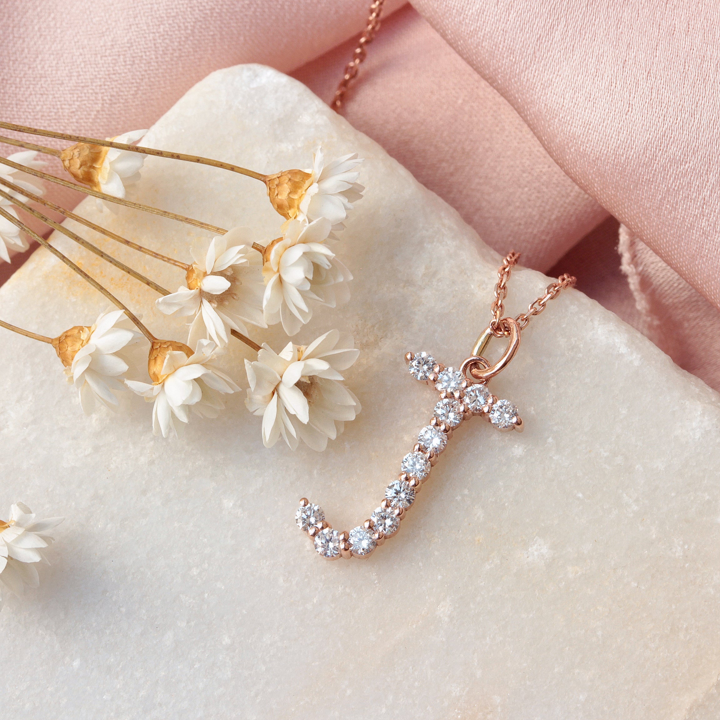 Jumbo Diamond Initial Charm 17mm Tall Rose gold necklace with diamond pendant on a marble surface with dried flowers.