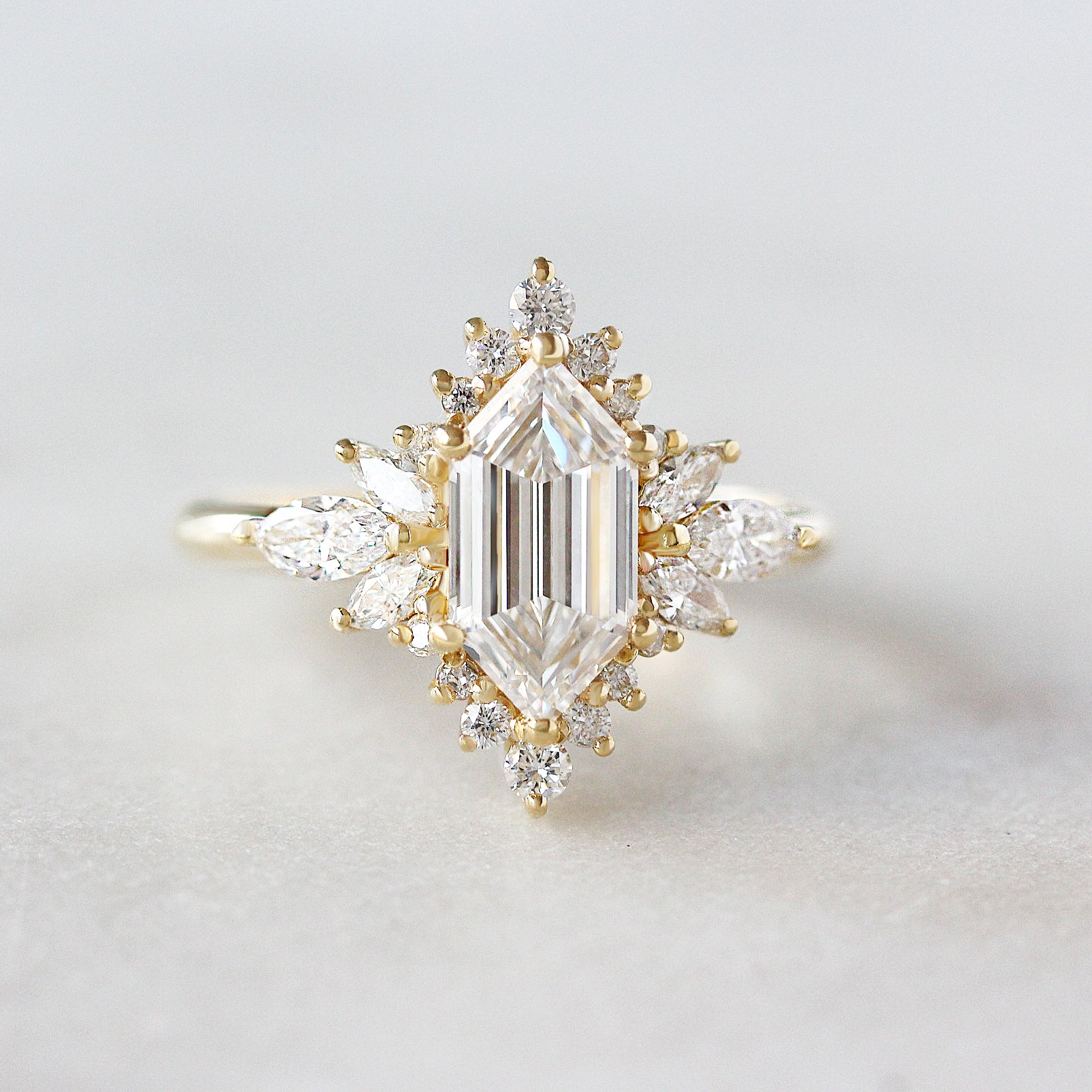 Diamond ring with a central emerald-cut diamond and smaller diamonds on a light gray background