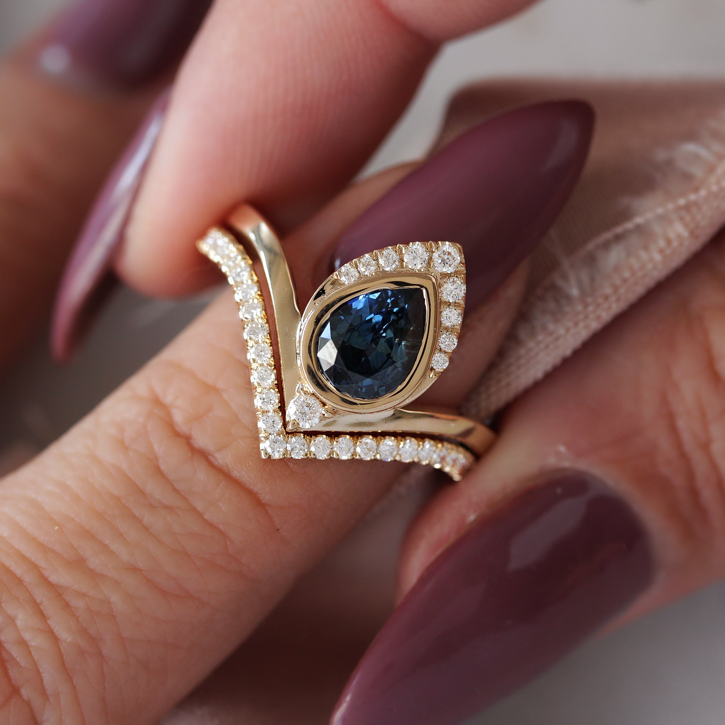 A pear-shaped teal sapphire engagement ring with a halo of white diamonds set in a yellow gold band, accompanied by a matching wedding band.
