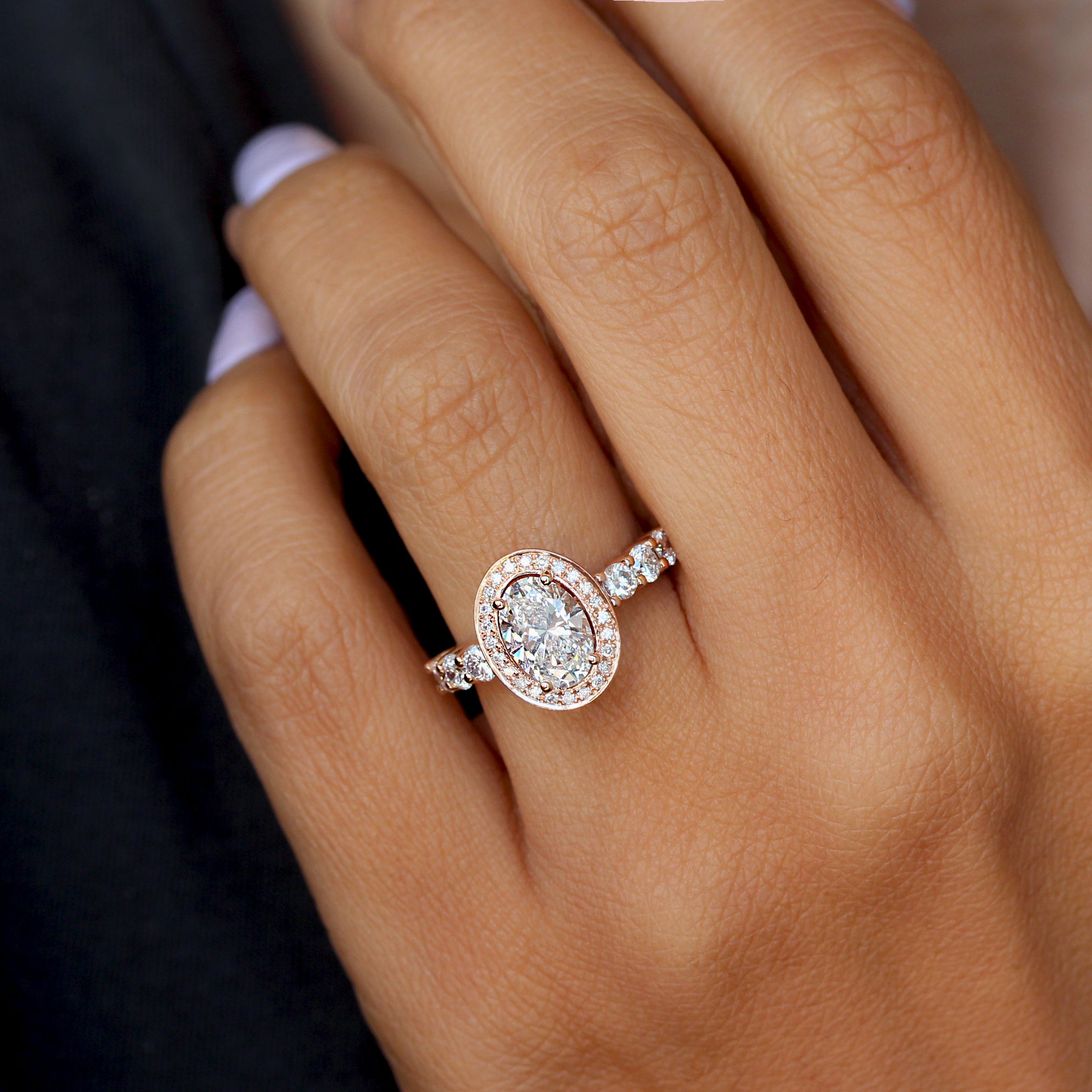 An oval diamond halo engagement ring with accent stones set in a yellow gold band, the center stone is large and prominently displayed, flanked by smaller stones on the sides.